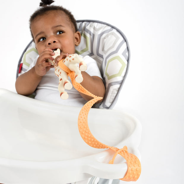 Baby product BooginHead SippiGrip Silicone in orange. Silicone strap holing toy to highchair. Easy to clean, bumps for soothing teething gums