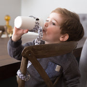 Toddler using BooginHead SippiGrip in Chevron to keep the sippy cup clean and attached to their chair. Size adjustable strap can attach to bottles, sippy cups or toys. Essential baby and toddler supply! Easy to clean. 